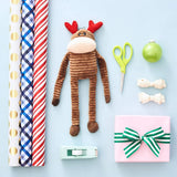 Decorative items including Large ZippyPaws Reindeer Holiday Crinkle Dog Toy, gift wrap, scissors, tape and a present on a light blue background