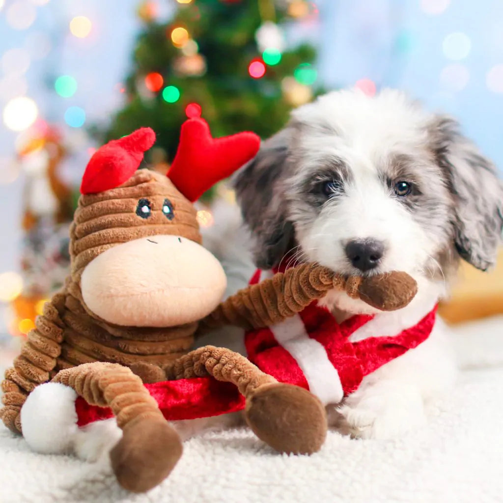 Dog playing with Small ZippyPaws Reindeer Holiday Crinkle Dog Toy in front of a decorated Christmas tree